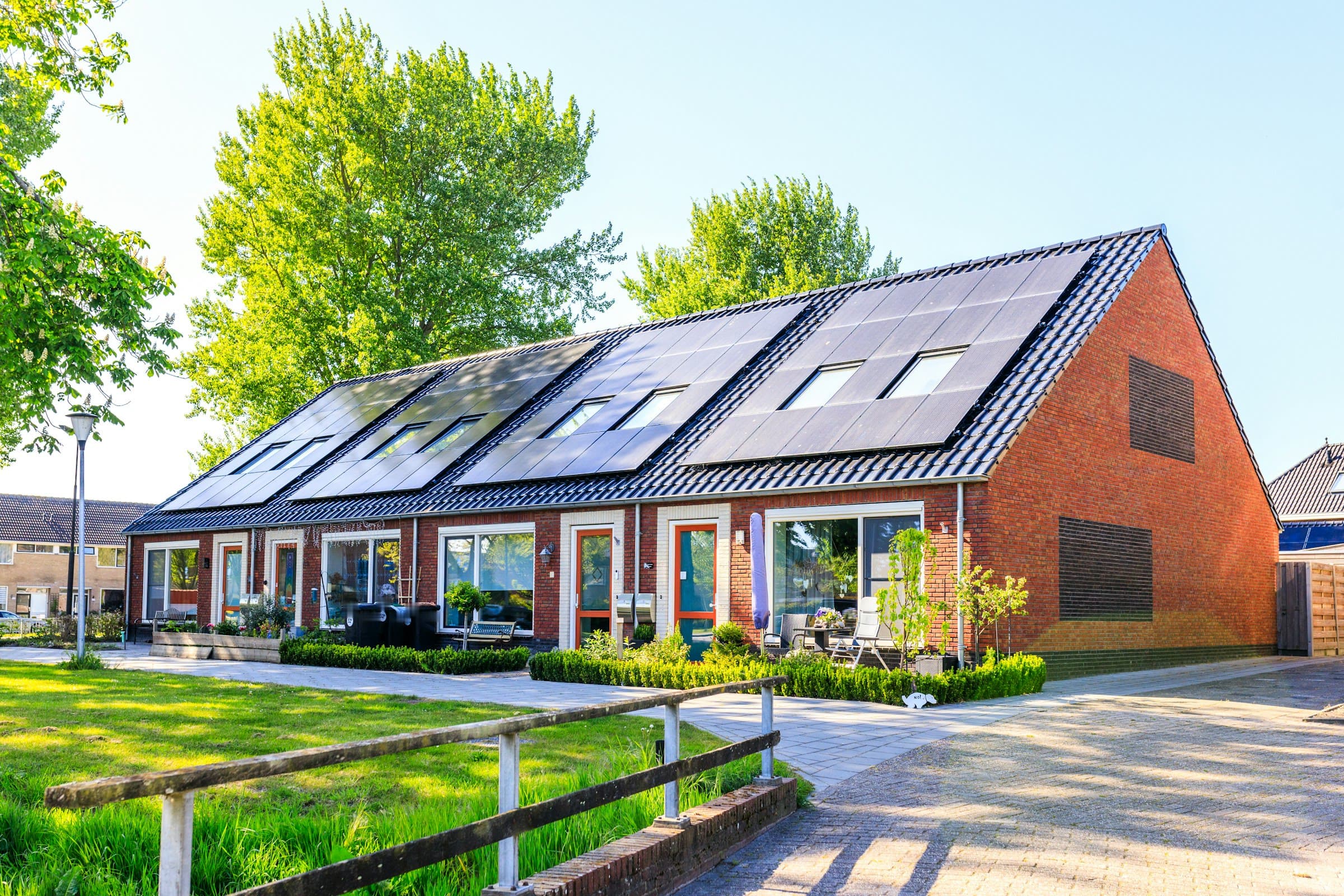 Rij bakstenen woningen met zwarte zonnepanelen over bijna het hele dak, op een heldere voorjaarsochtend