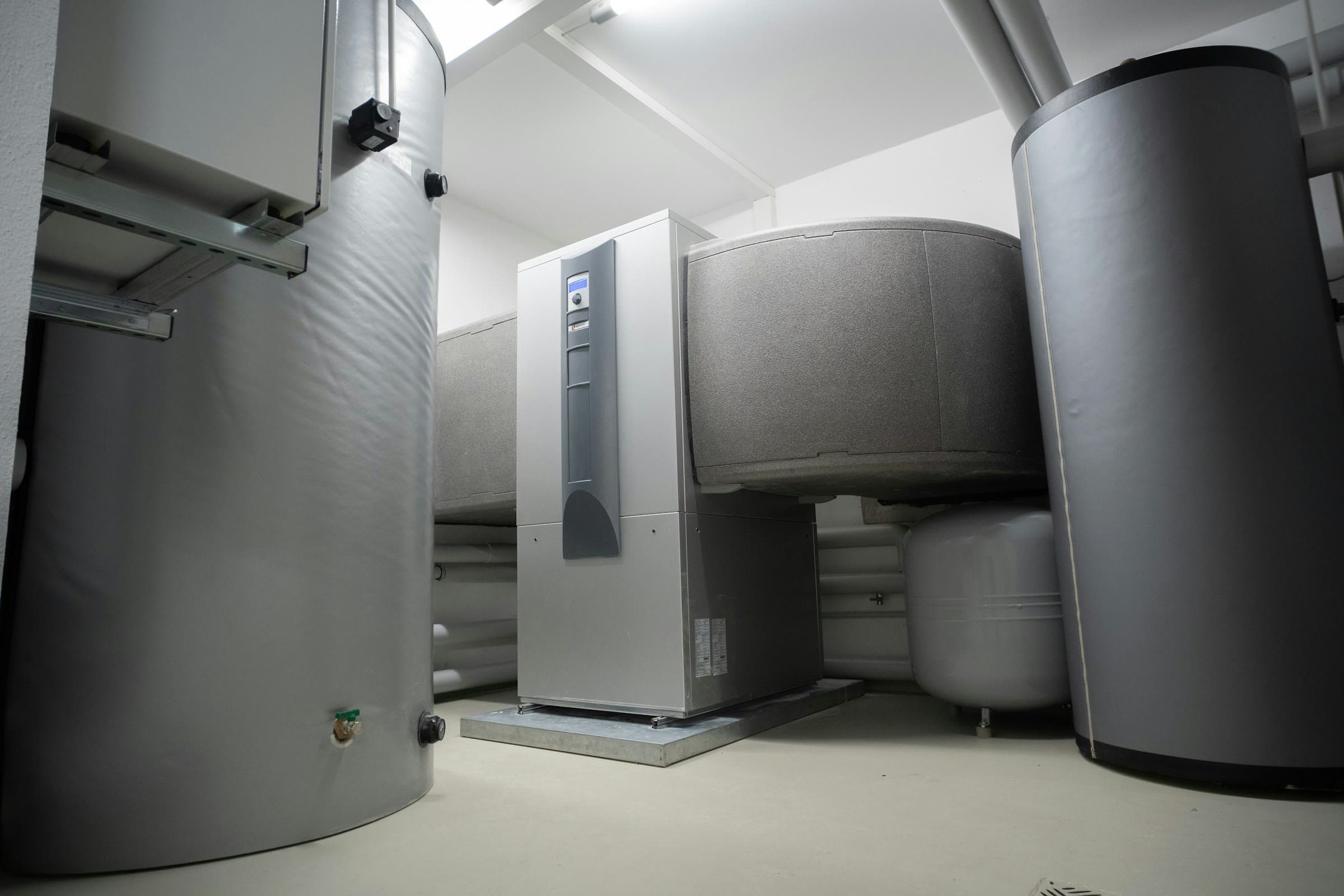Technische ruimte met een binnenunit van een warmtepomp tussen een boilervat en een buffervat met isolatiemantel